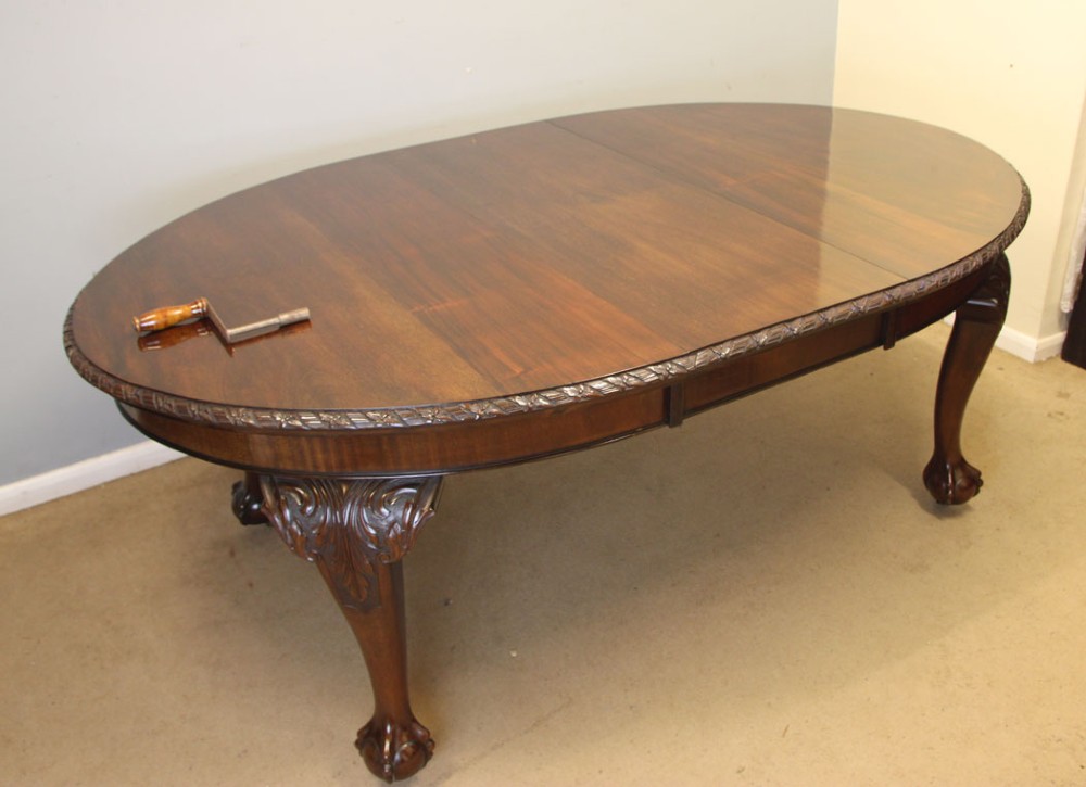 An oval mahogany extending dining table with two insert leaves, carved border edging, cabriole legs featuring acanthus knee carvings, and ball-and-claw feet. View IV