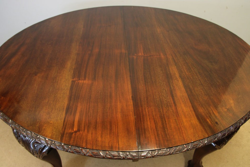 An oval mahogany extending dining table with two insert leaves, carved border edging, cabriole legs featuring acanthus knee carvings, and ball-and-claw feet. View V