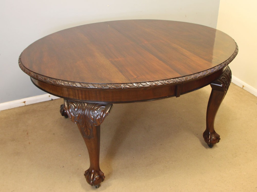 An oval mahogany extending dining table with two insert leaves, carved border edging, cabriole legs featuring acanthus knee carvings, and ball-and-claw feet. View VII