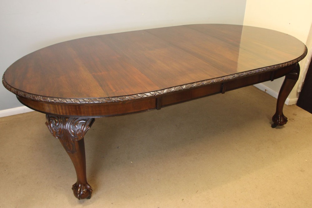 An oval mahogany extending dining table with two insert leaves, carved border edging, cabriole legs featuring acanthus knee carvings, and ball-and-claw feet. View IX
