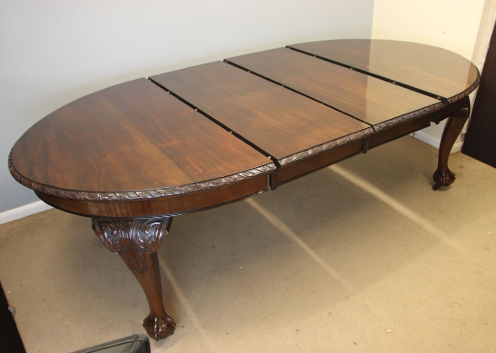 An oval mahogany extending dining table with two insert leaves, carved border edging, cabriole legs featuring acanthus knee carvings, and ball-and-claw feet. View XI