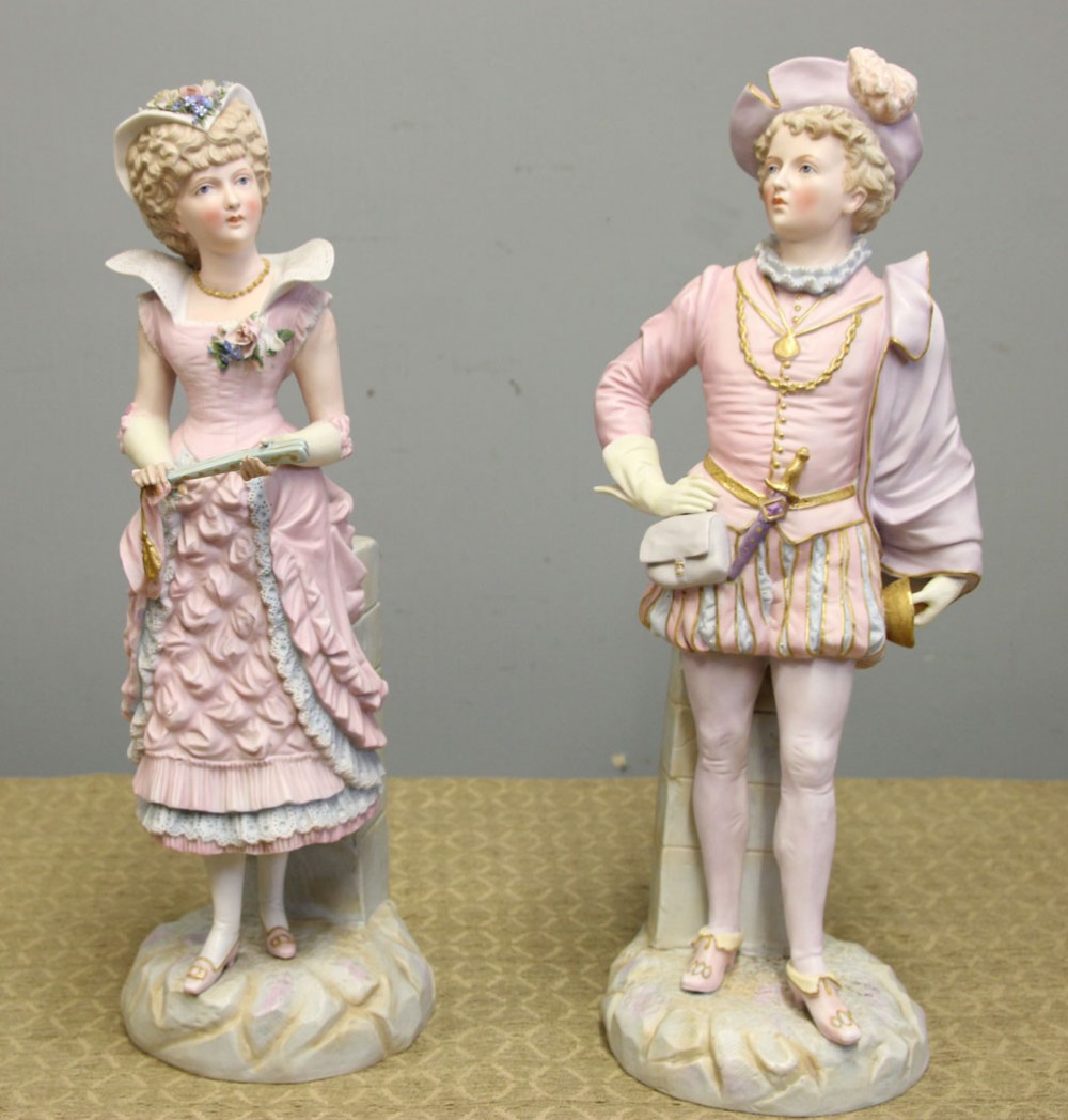 A pair of antique matte bisque porcelain figurines depicting a lady and gentleman dressed in pastel pink eighteenth-century period costume.