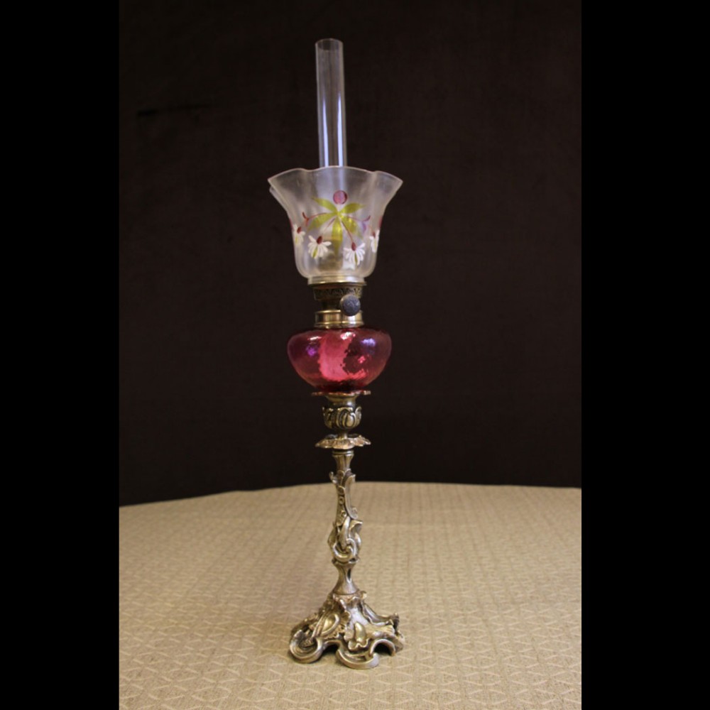 An antique Victorian peg oil lamp featuring a cast brass base, a red cranberry glass font, a painted frosted tulip glass shade, and a clear chimney.