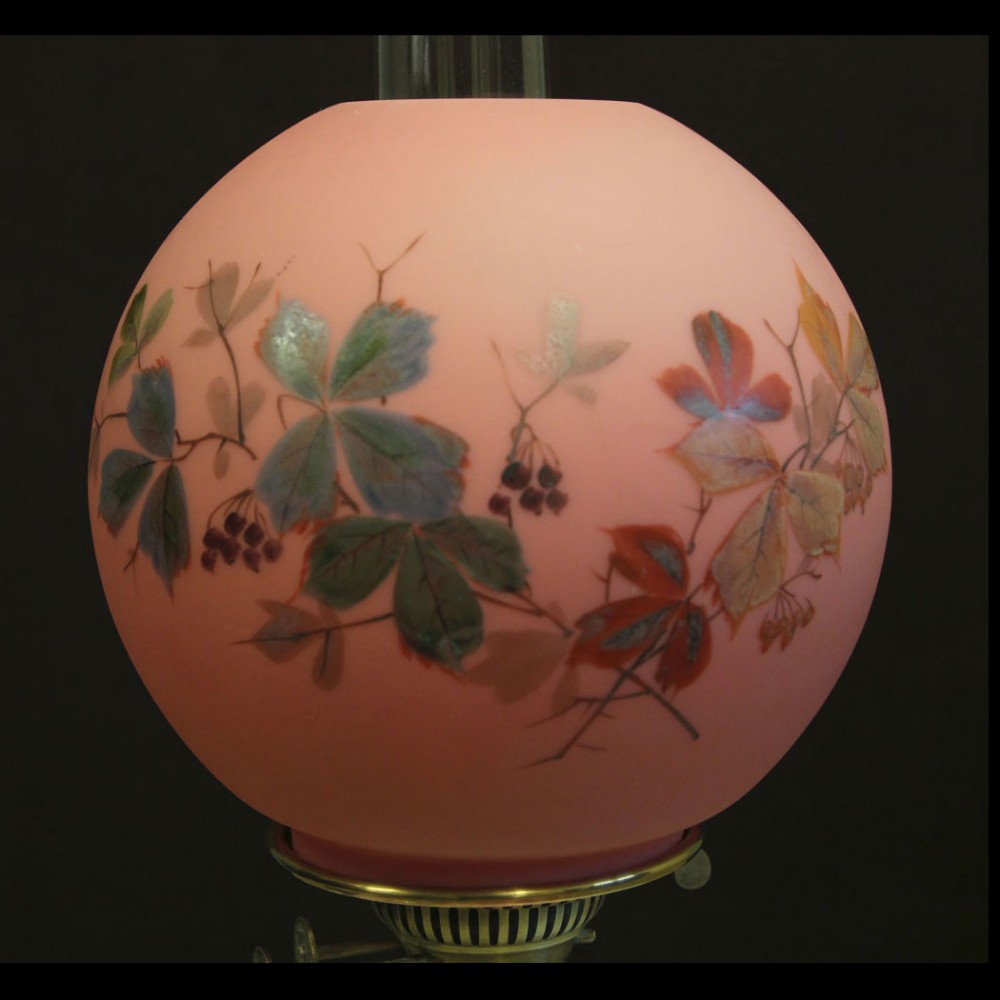 A spherical pink satin glass oil lamp shade hand-painted with autumn leaves and dark berries.