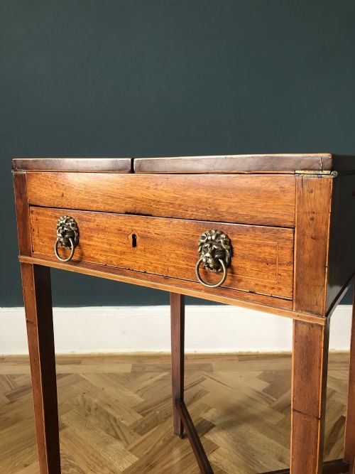 fig 1. An antique Regency mahogany fold-out games table featuring a hinged top, a front drawer with brass lion-mask ring handles, tapered square legs, an X-stretcher base, and small castors.