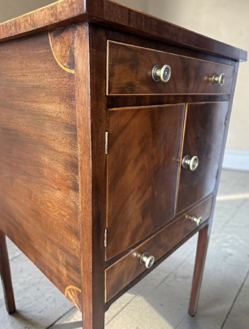 A Georgian flame mahogany bedside cabinet featuring a top drawer, central double doors, and a bottom drawer, supported by square tapered legs. View V