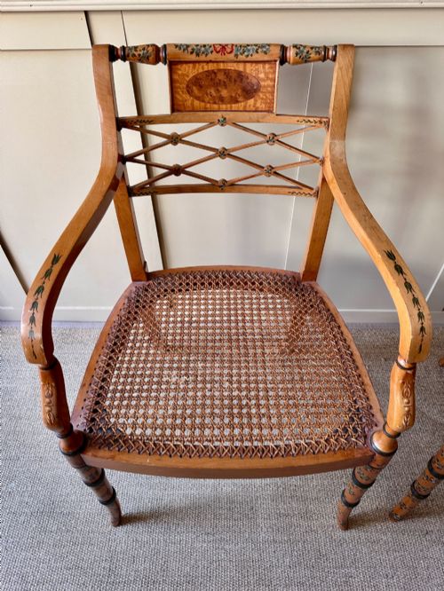 fig 2. A pair of Edwardian Sheraton Revival painted wooden elbow chairs featuring woven cane seats, lattice backrests, and floral painted decoration.