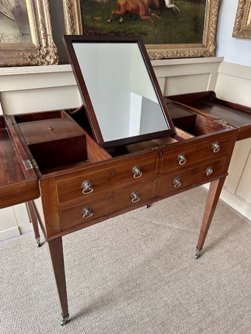 fig 3. A late Georgian mahogany gentlemans dressing table featuring two hinged side leaves open to reveal internal compartments and a central adjustable mirror, raised on square tapered legs with brass castors.