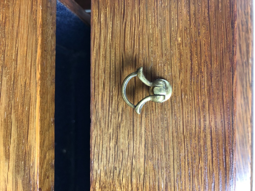 An Edwardian medium oak tabletop cabinet featuring twin glazed doors, six interior drawers with brass teardrop handles, and a central keyhole with key. View IV