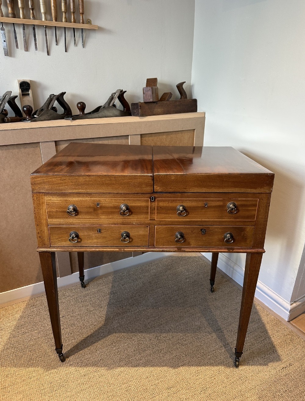 A late Georgian mahogany gentlemans dressing table with a split hinged fold-over top, drawer fronts with brass handles, and tapered square legs on castors.