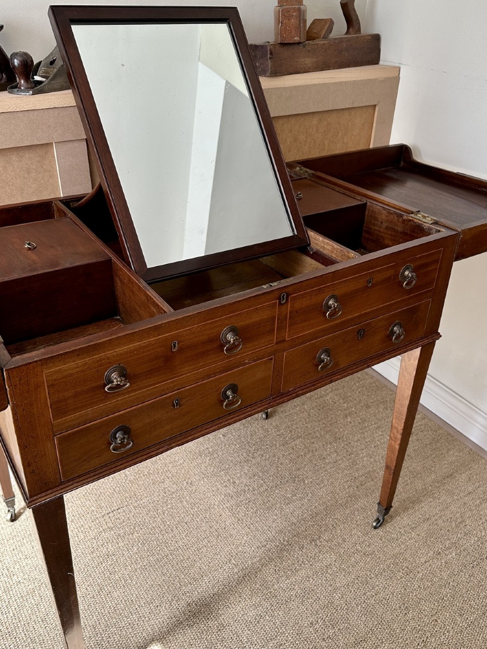 A late Georgian mahogany gentlemans dressing table with a split hinged fold-over top, drawer fronts with brass handles, and tapered square legs on castors. View II
