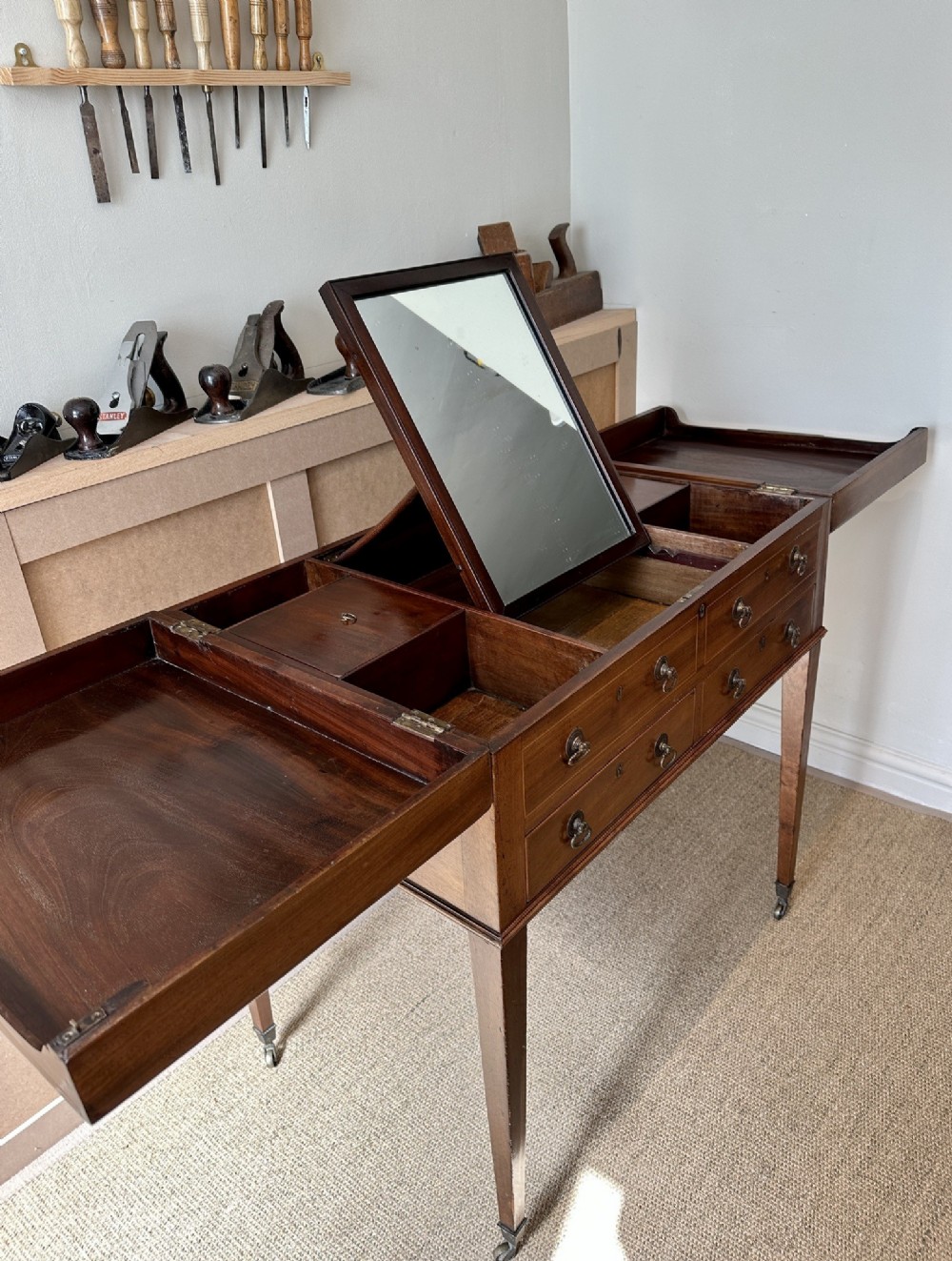 A late Georgian mahogany gentlemans dressing table with a split hinged fold-over top, drawer fronts with brass handles, and tapered square legs on castors. View III