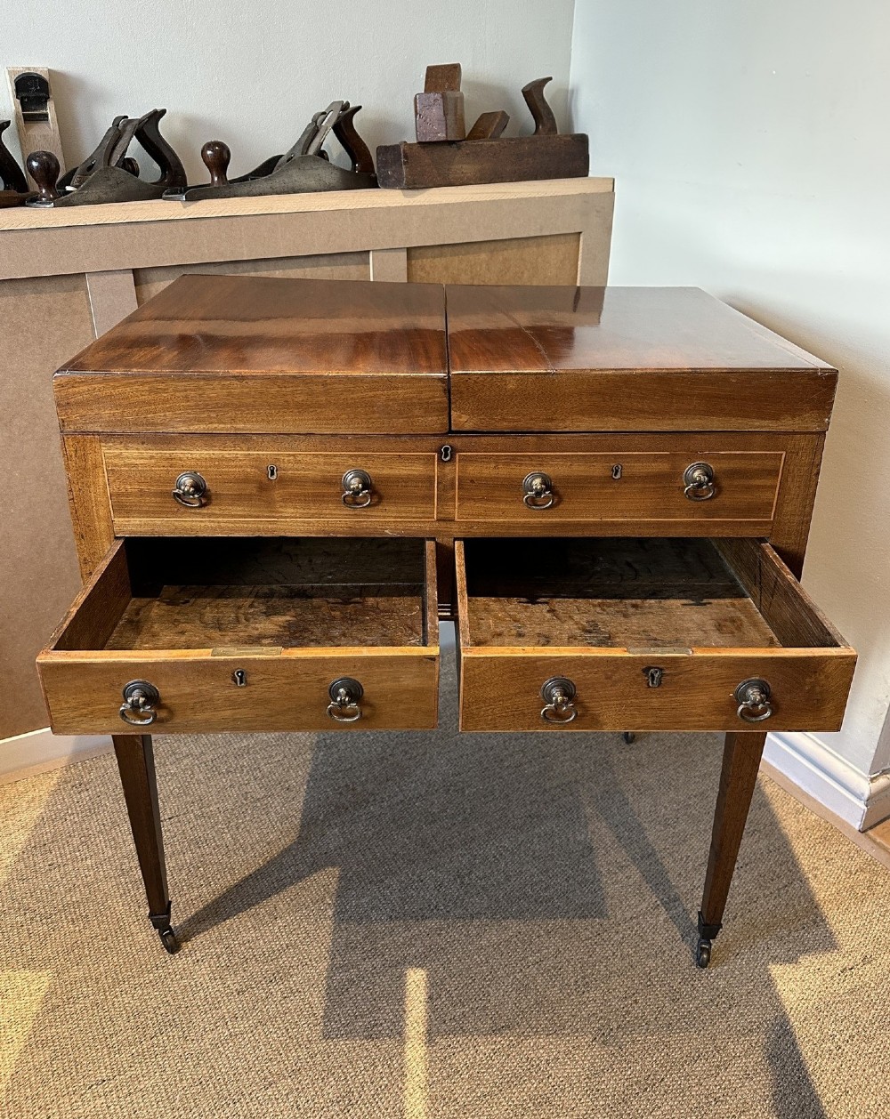 A late Georgian mahogany gentlemans dressing table with a split hinged fold-over top, drawer fronts with brass handles, and tapered square legs on castors. View IV