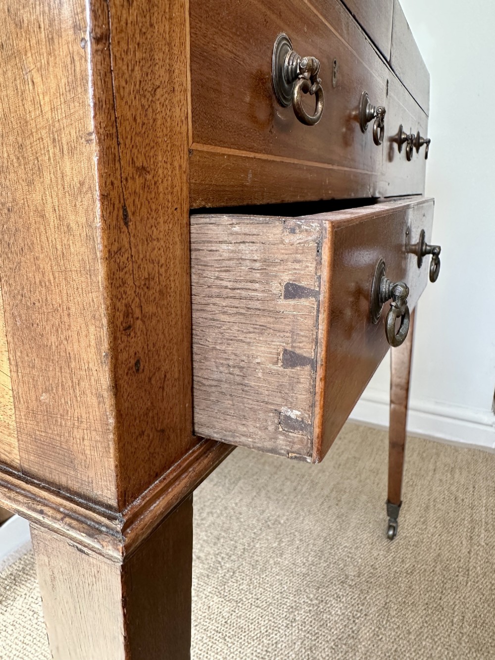 A late Georgian mahogany gentlemans dressing table with a split hinged fold-over top, drawer fronts with brass handles, and tapered square legs on castors. View V