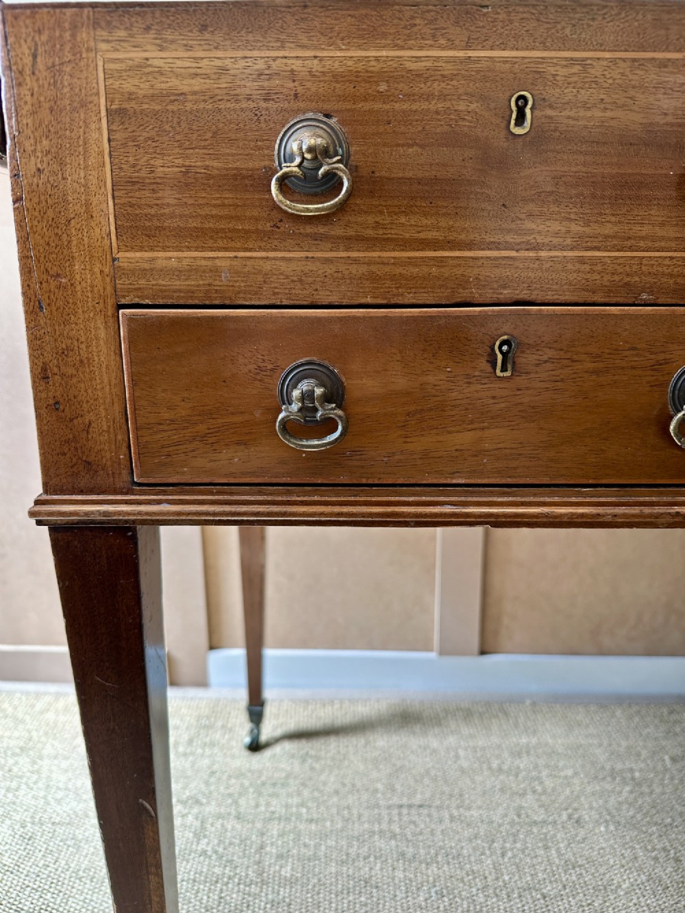 A late Georgian mahogany gentlemans dressing table with a split hinged fold-over top, drawer fronts with brass handles, and tapered square legs on castors. View VI