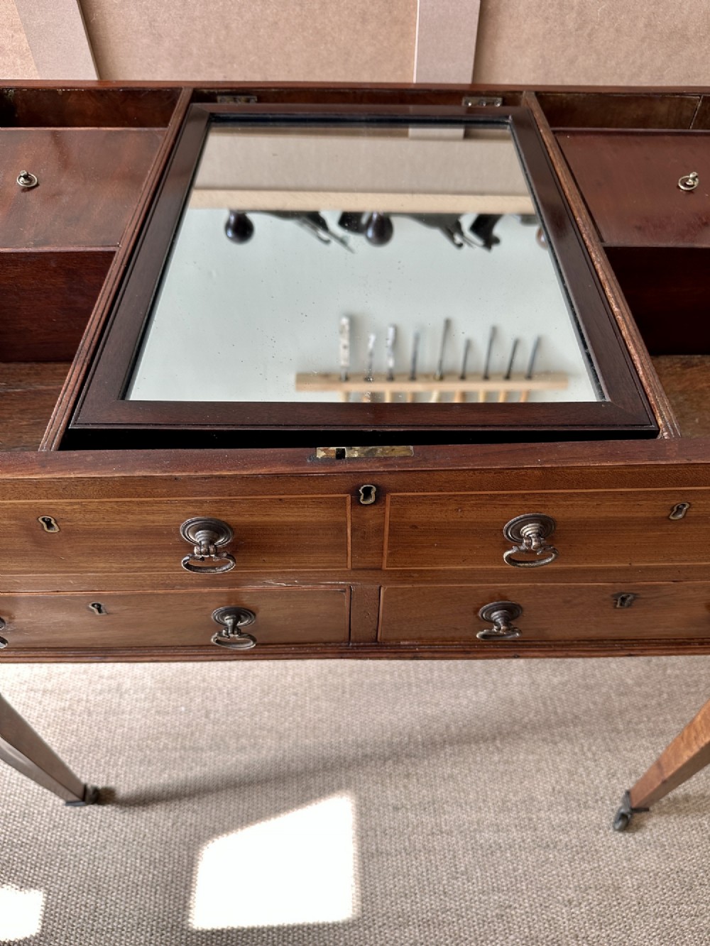 A late Georgian mahogany gentlemans dressing table with a split hinged fold-over top, drawer fronts with brass handles, and tapered square legs on castors. View VII