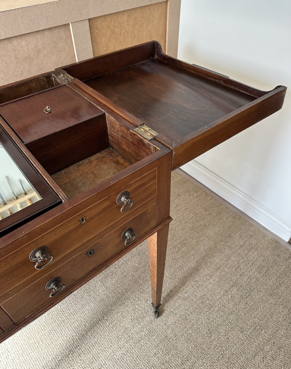 A late Georgian mahogany gentlemans dressing table with a split hinged fold-over top, drawer fronts with brass handles, and tapered square legs on castors. View VIII
