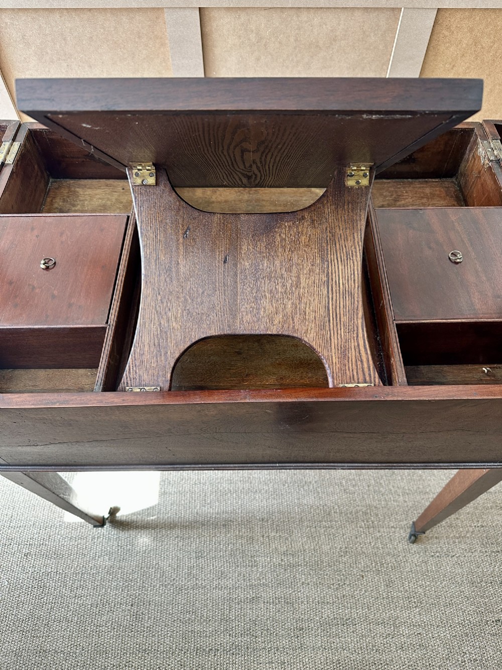 A late Georgian mahogany gentlemans dressing table with a split hinged fold-over top, drawer fronts with brass handles, and tapered square legs on castors. View IX