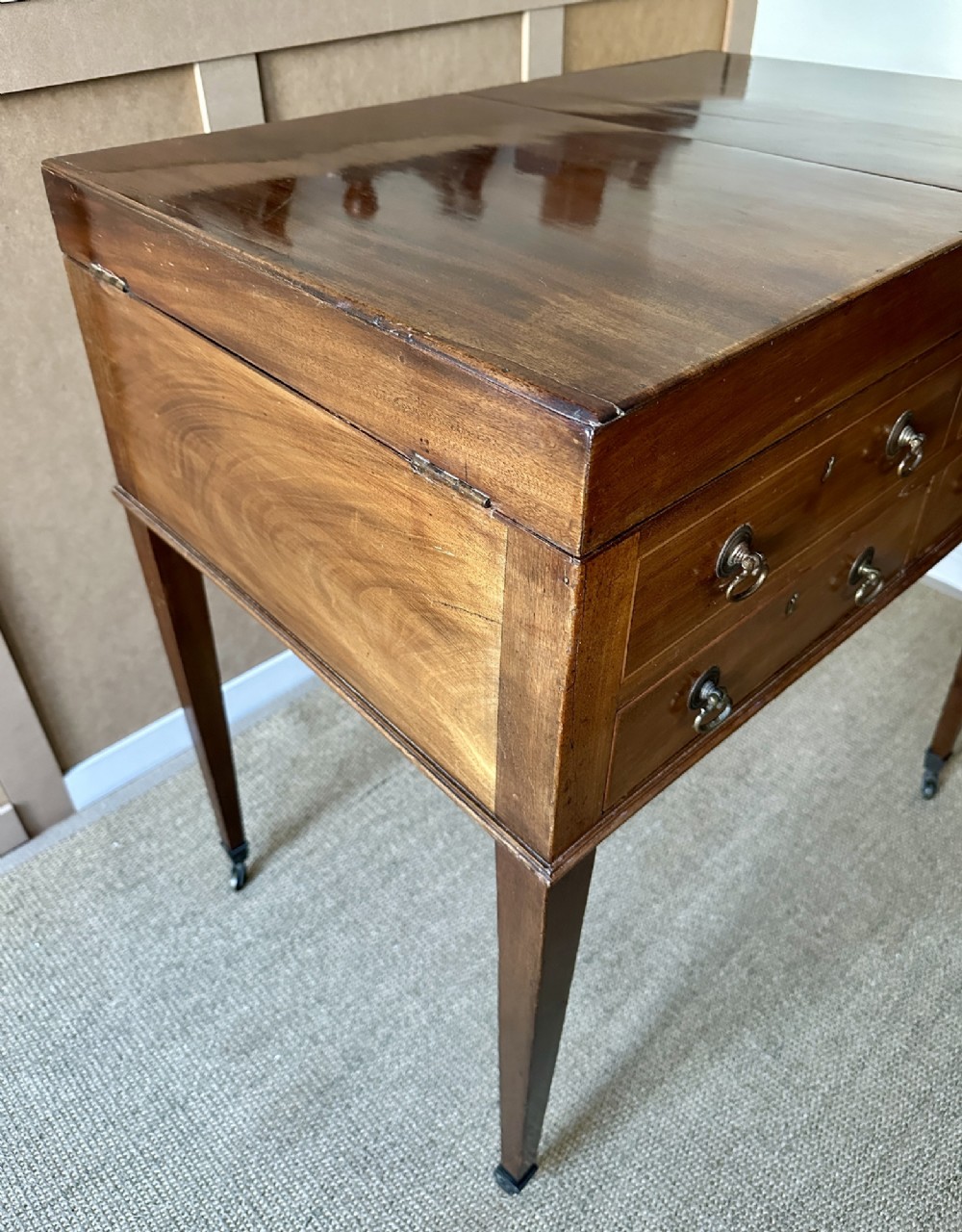 A late Georgian mahogany gentlemans dressing table with a split hinged fold-over top, drawer fronts with brass handles, and tapered square legs on castors. View X