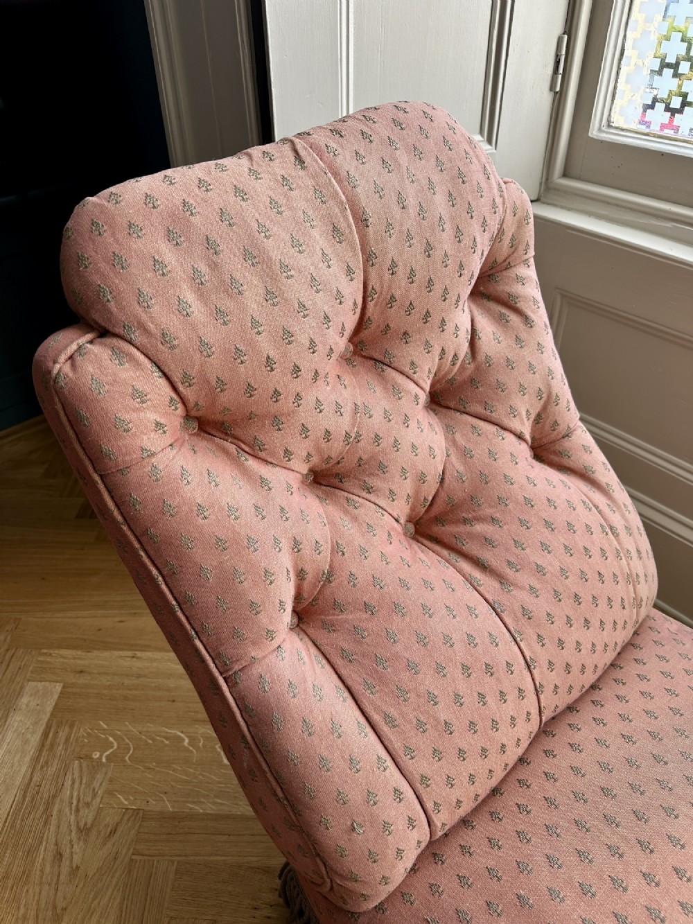A 19th-century low armless slipper chair upholstered in a patterned dusty pink fabric featuring button tufting on the backrest and dense fringe along the base. View III