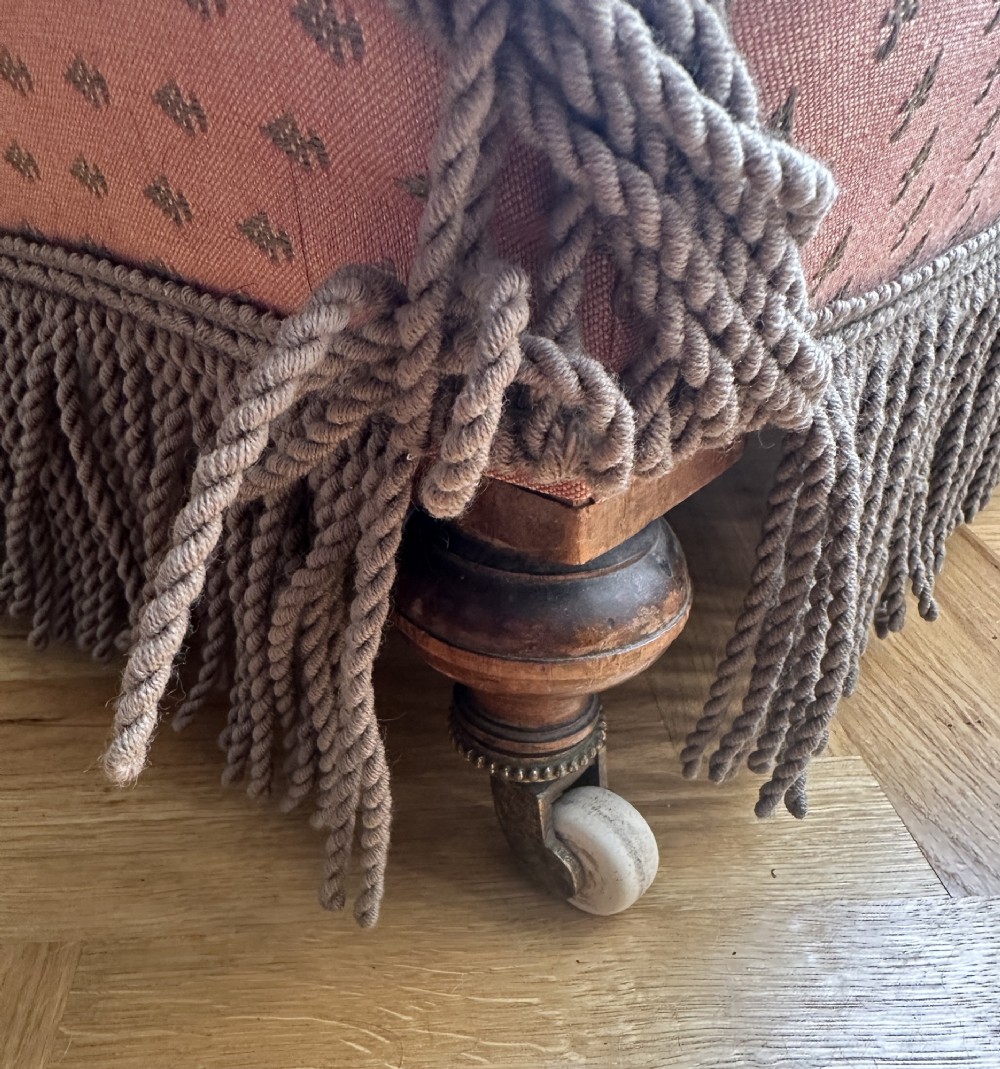 A 19th-century low armless slipper chair upholstered in a patterned dusty pink fabric featuring button tufting on the backrest and dense fringe along the base. View IV