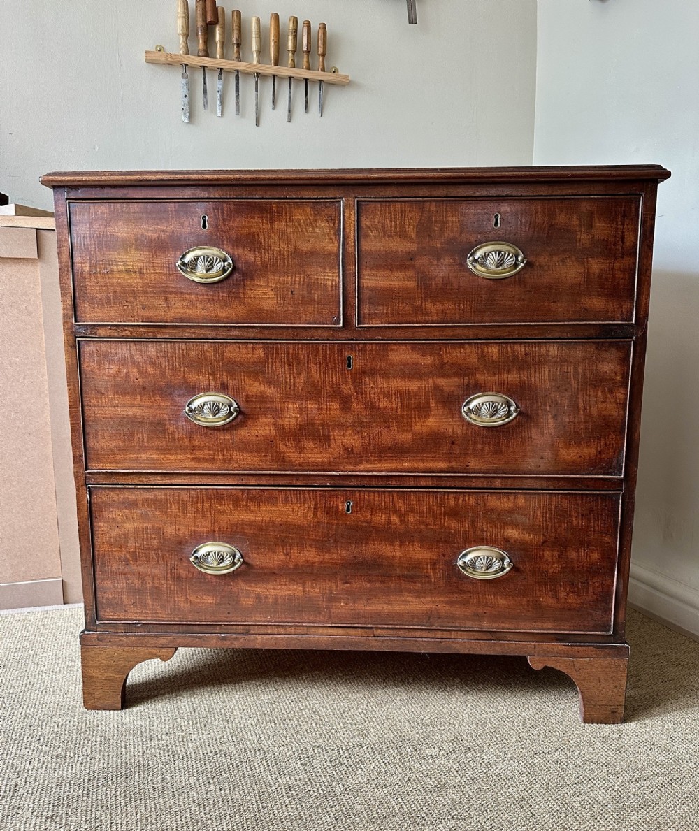 An antique warm brown mahogany chest of drawers featuring two short drawers over two long drawers with brass oval handles and bracket feet.