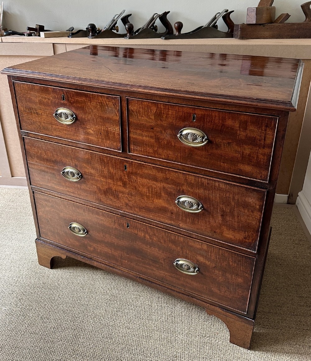 An antique warm brown mahogany chest of drawers featuring two short drawers over two long drawers with brass oval handles and bracket feet. View IV