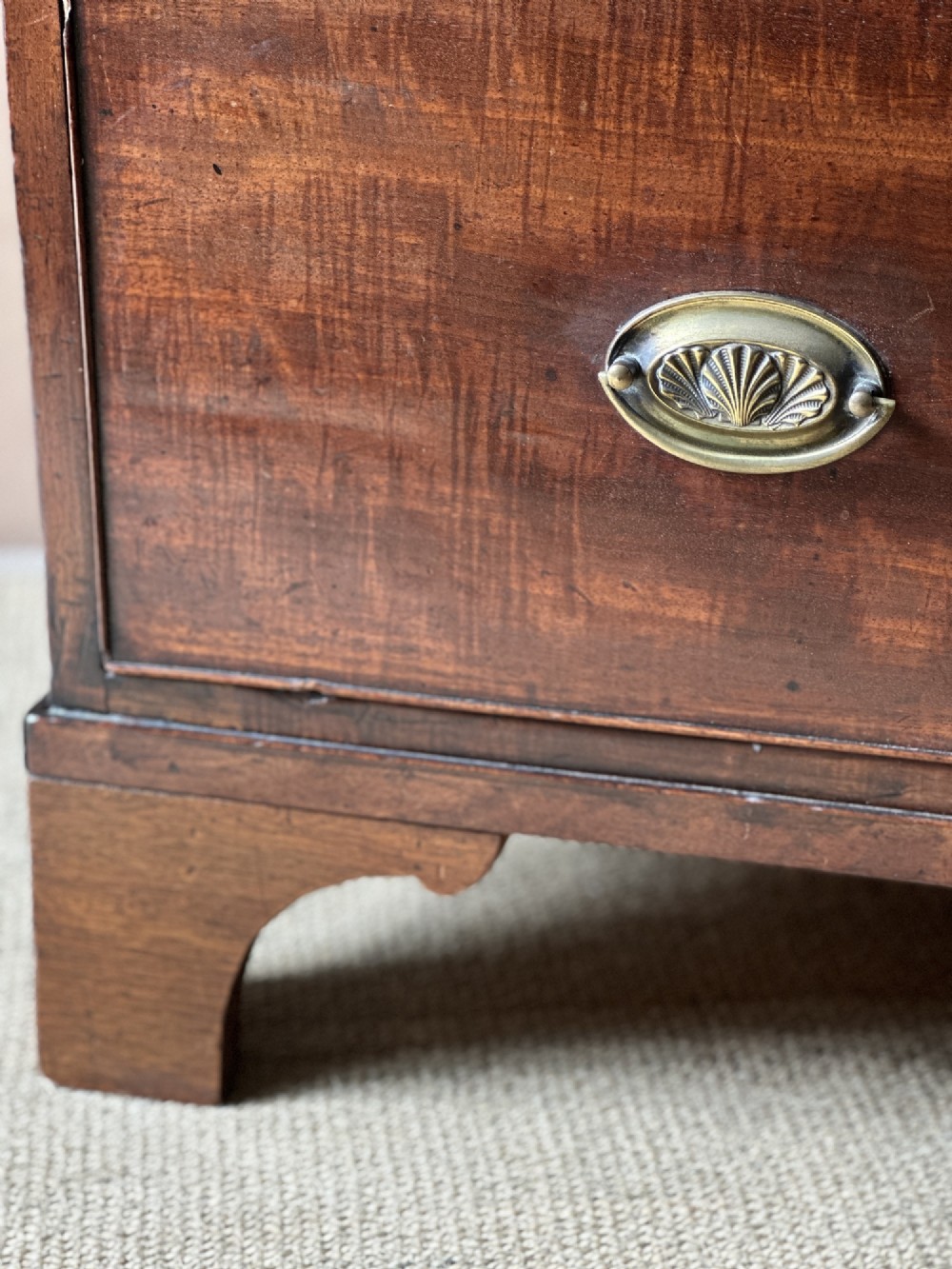An antique warm brown mahogany chest of drawers featuring two short drawers over two long drawers with brass oval handles and bracket feet. View V