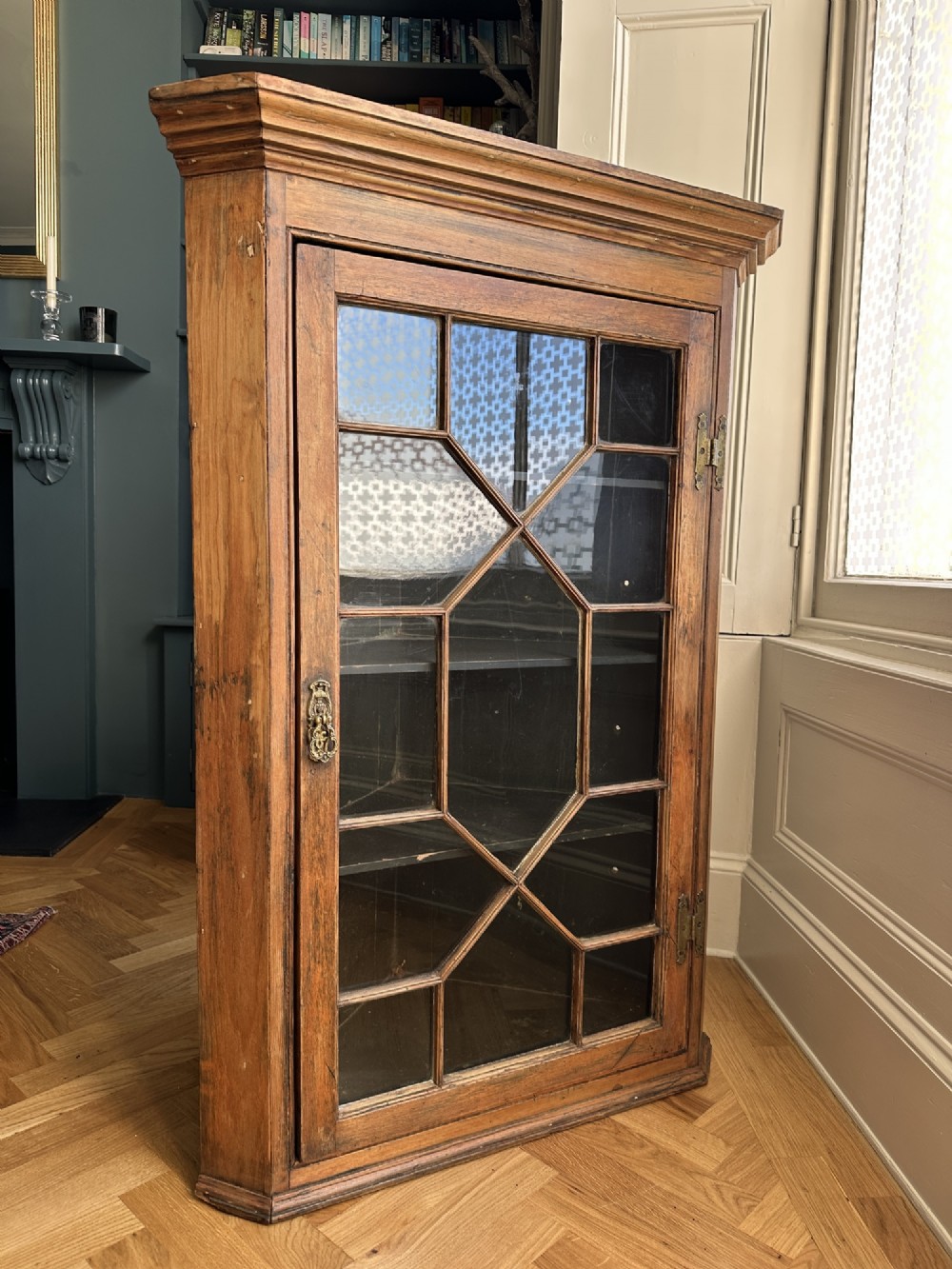 An antique stripped pine corner cabinet featuring a single glazed door with geometric astragal glazing bars and a dark painted interior.