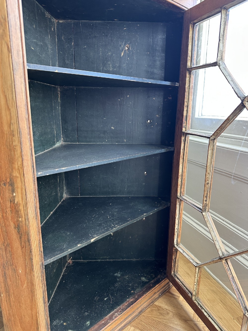 An antique stripped pine corner cabinet featuring a single glazed door with geometric astragal glazing bars and a dark painted interior. View II