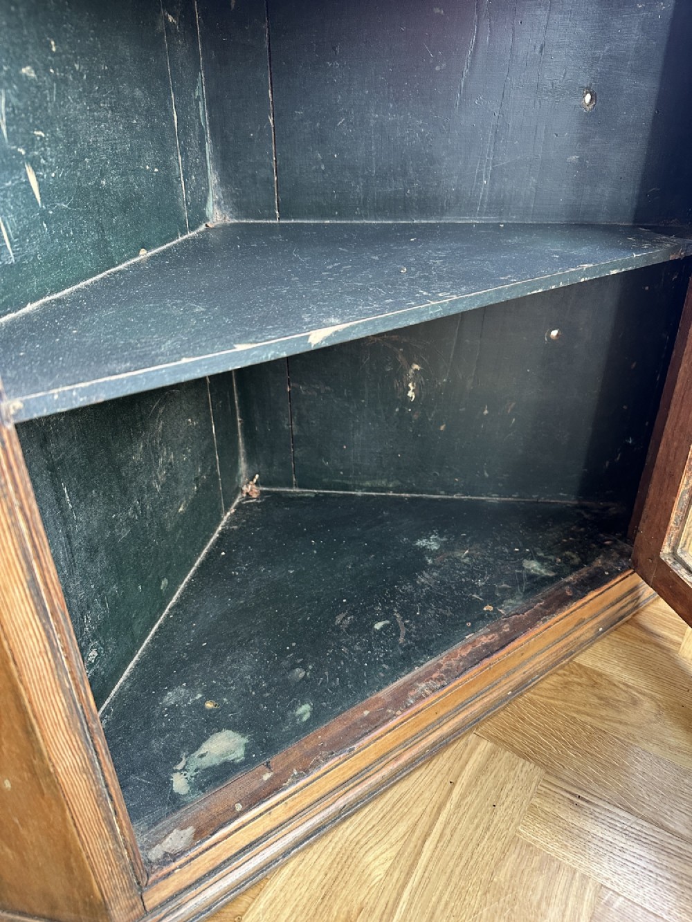 An antique stripped pine corner cabinet featuring a single glazed door with geometric astragal glazing bars and a dark painted interior. View VII