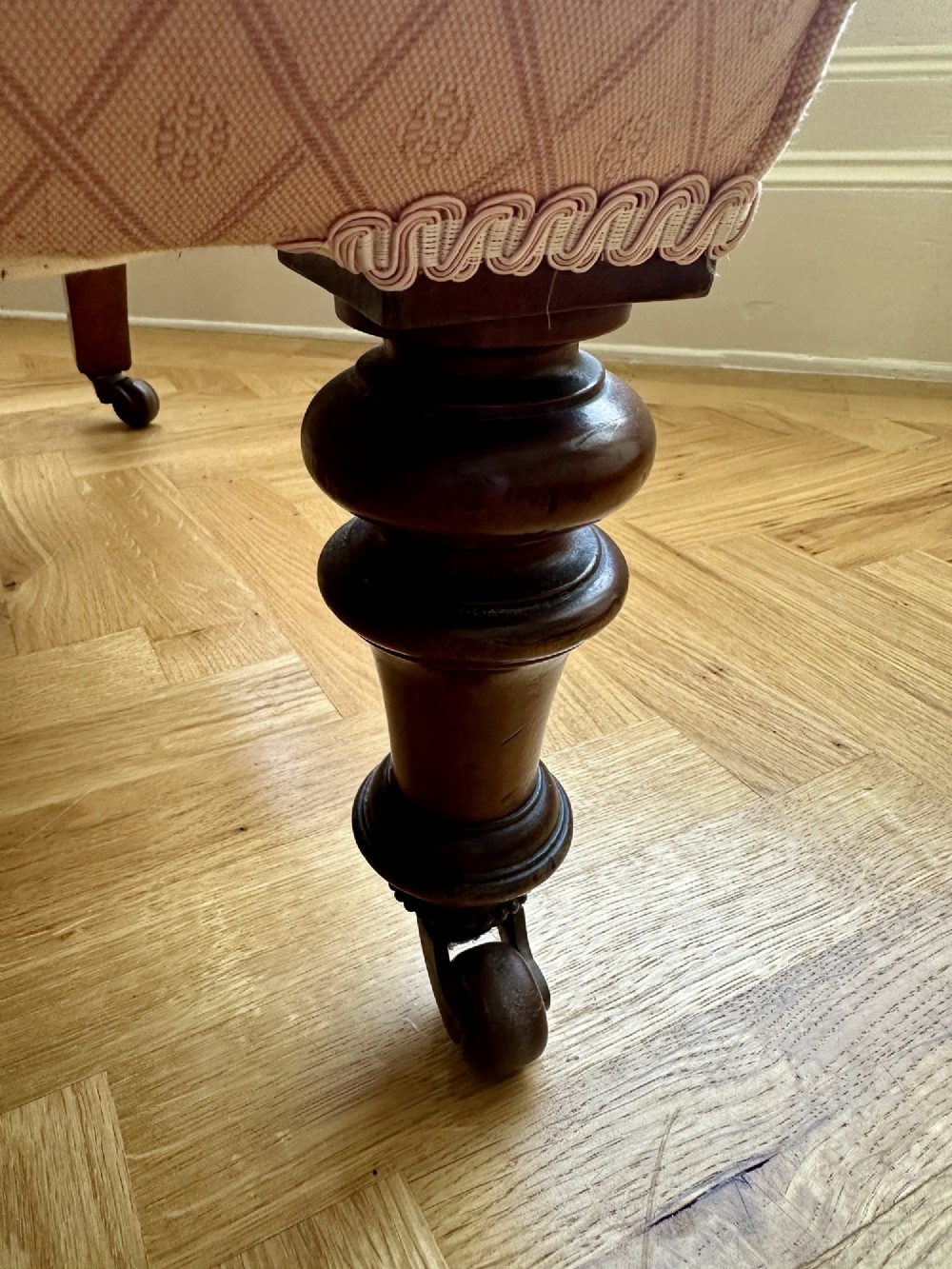 A low-seated Victorian slipper chair upholstered in dusty pink patterned fabric featuring a button-back design and turned dark timber legs with brass castors. View III