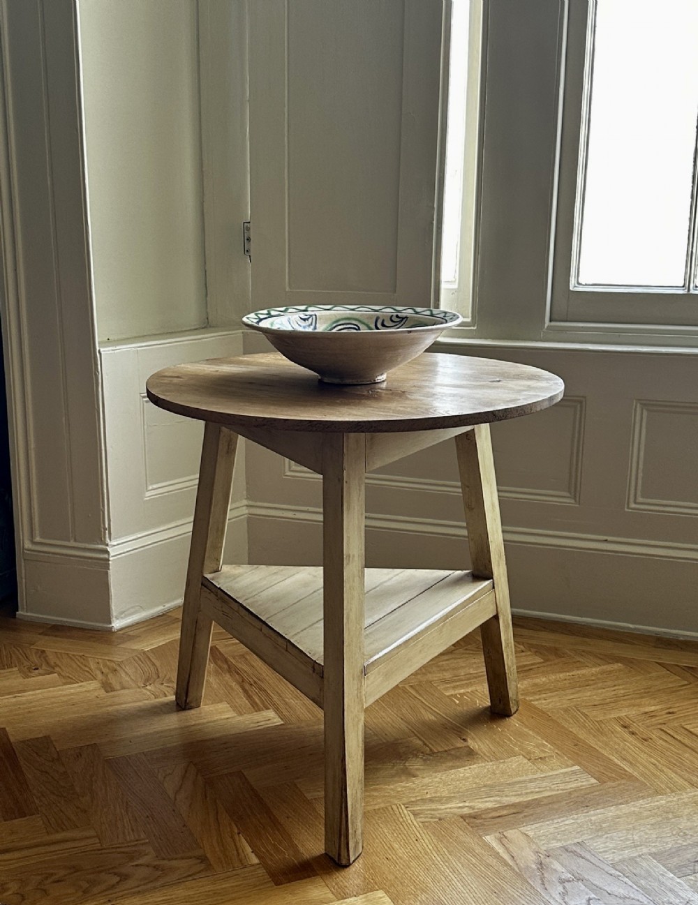 A rustic elm cricket table featuring a circular top, three splayed legs, and a lower triangular shelf.