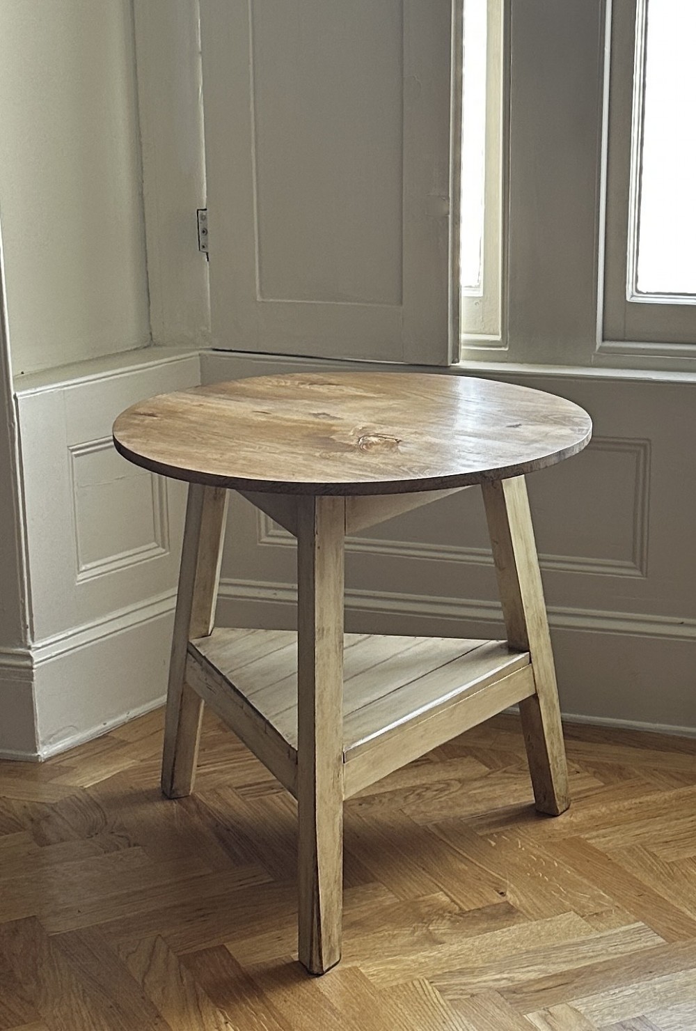 A rustic elm cricket table featuring a circular top, three splayed legs, and a lower triangular shelf. View II