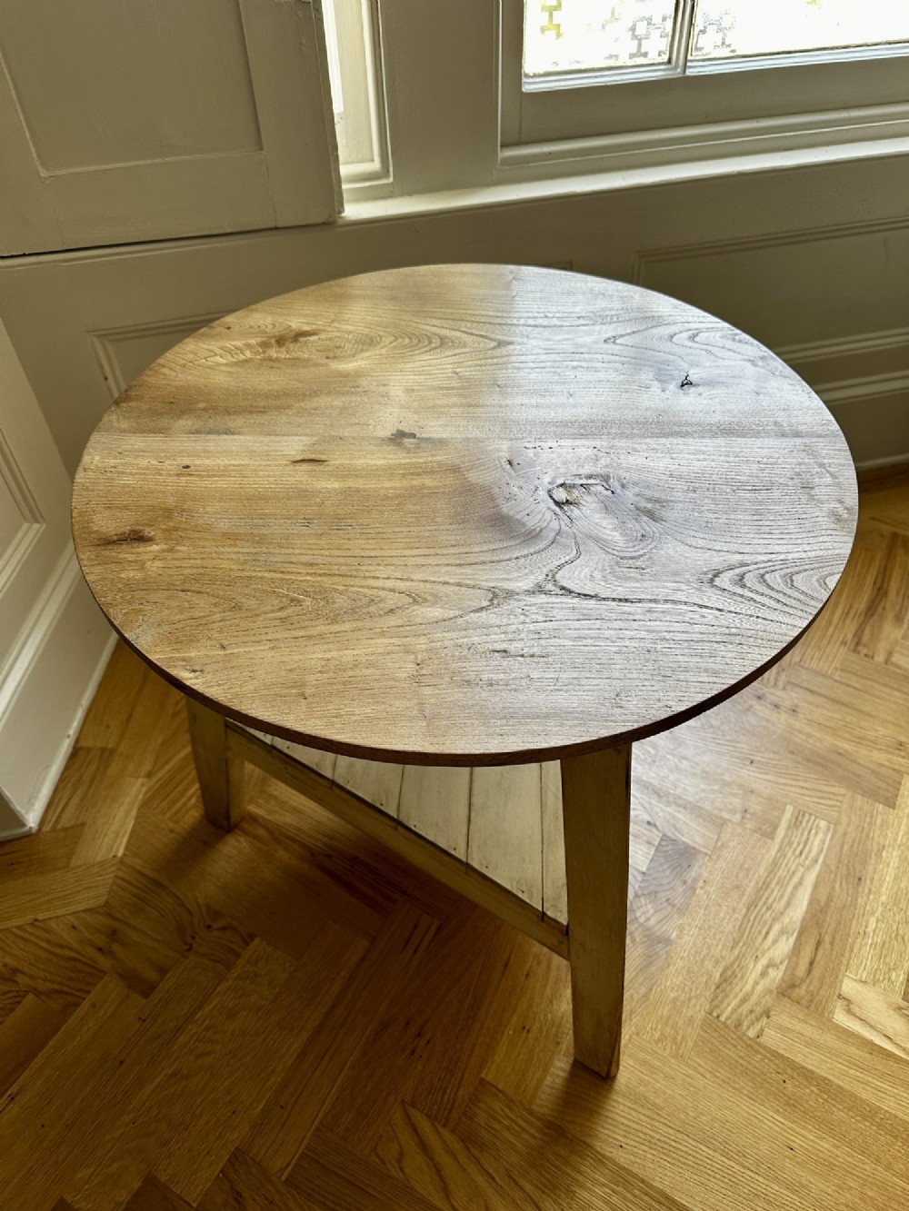 A rustic elm cricket table featuring a circular top, three splayed legs, and a lower triangular shelf. View V