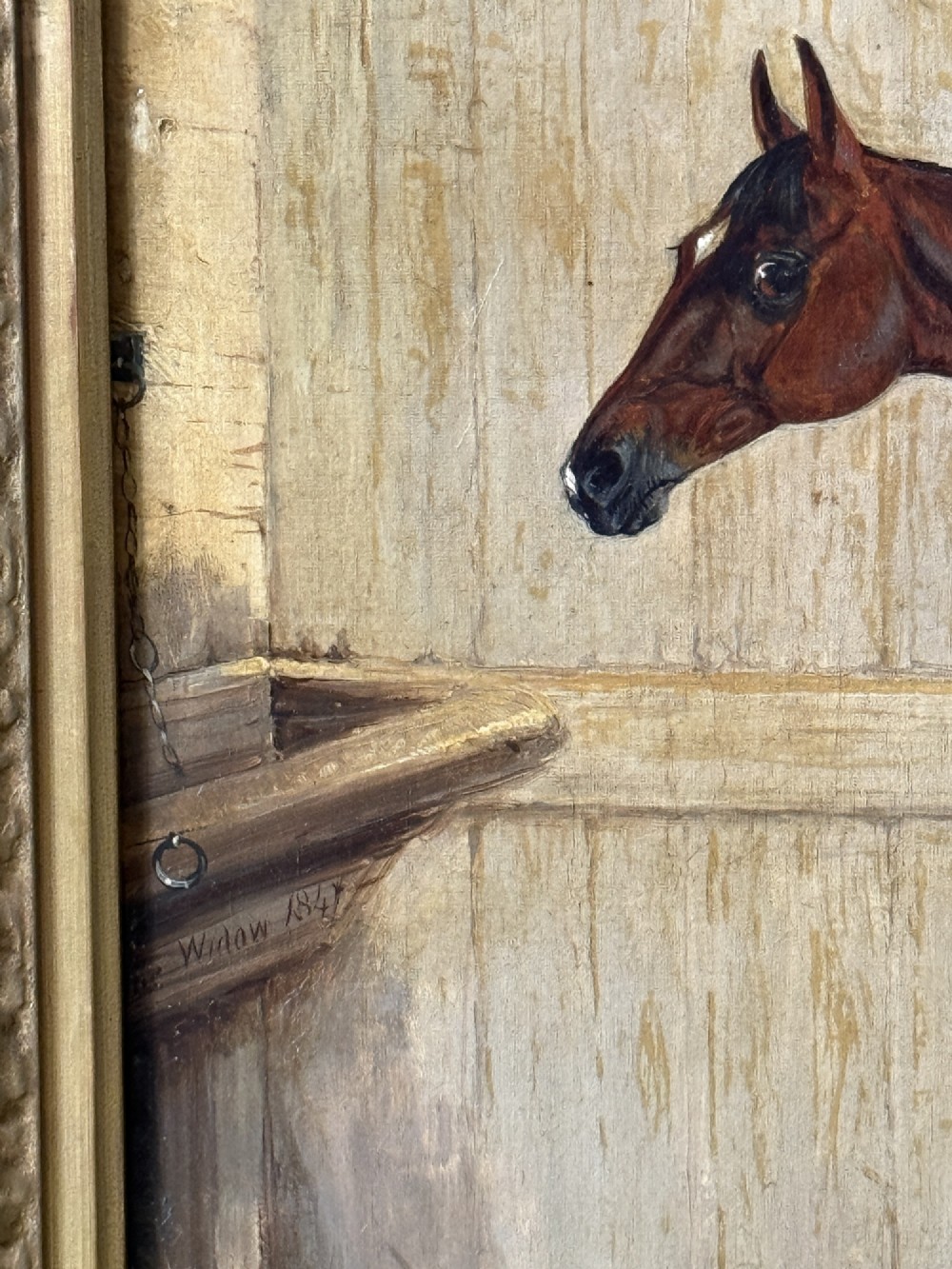 A Victorian oil painting depicting a brown racehorse standing in a straw-filled stable stall within a gilded frame. View IV