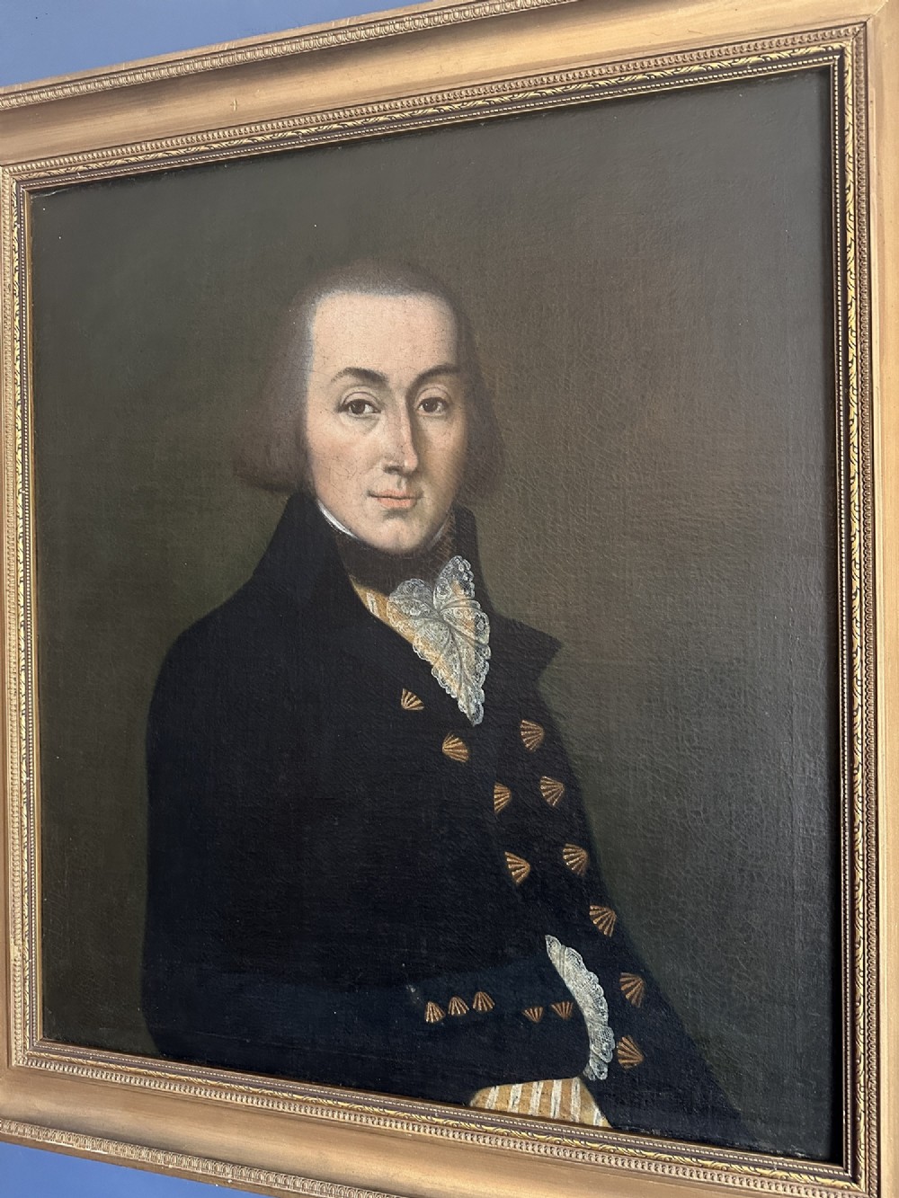 A late Georgian oil portrait of a gentleman in a dark coat with a white lace cravat set inside a giltwood frame.