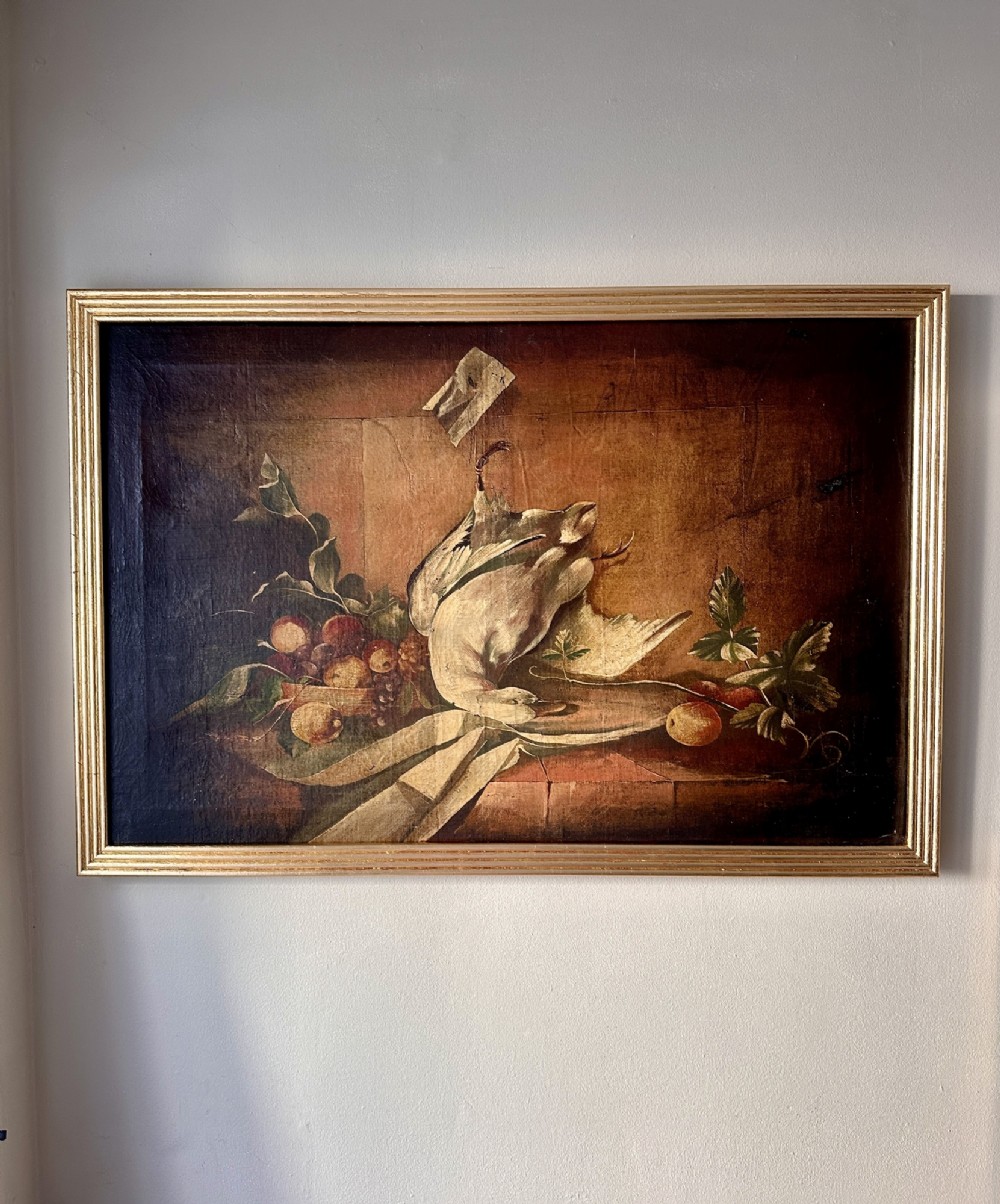 A 19th-century Continental school oil painting depicting hanging game birds and fruit arranged on a stone ledge within a gilded frame.