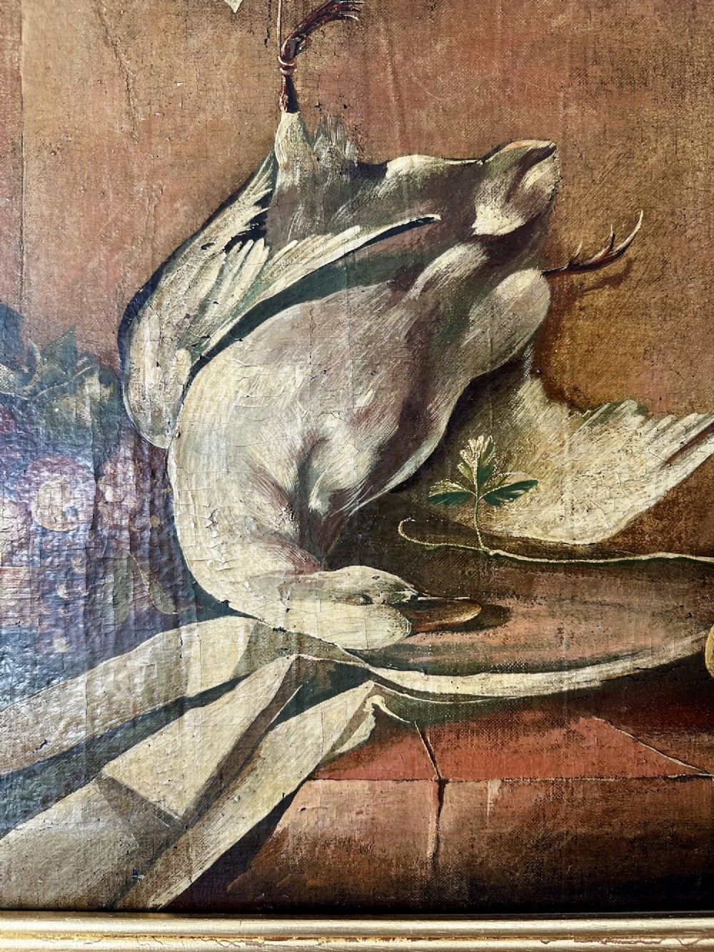 A 19th-century Continental school oil painting depicting hanging game birds and fruit arranged on a stone ledge within a gilded frame. View II