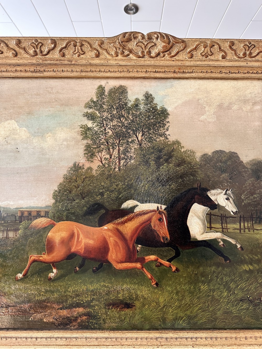 A 19th-century oil painting on canvas depicting three galloping horses in a landscape with a steam train in the background, framed in an ornate gilded wood frame. View II