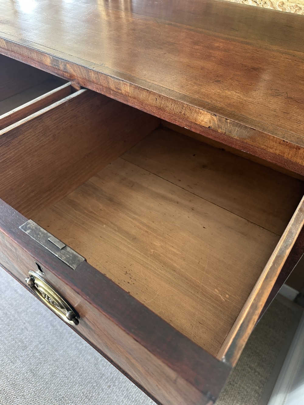 A late Georgian flame mahogany chest of drawers featuring a two-over-three drawer configuration, brass oval handles, bracket feet, and a polished wood finish. View VII