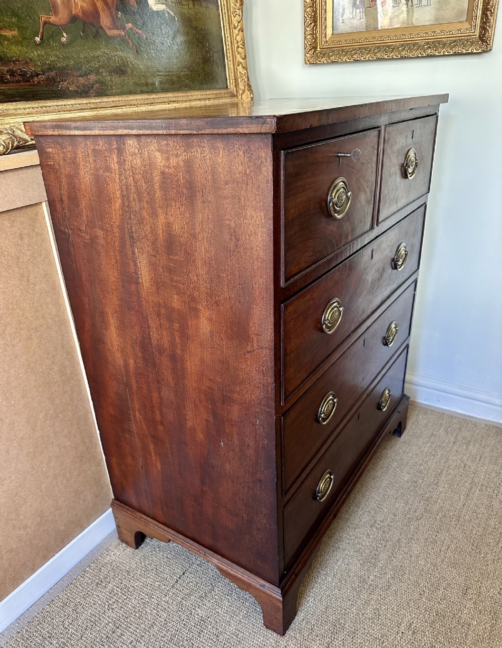 A late Georgian flame mahogany chest of drawers featuring a two-over-three drawer configuration, brass oval handles, bracket feet, and a polished wood finish. View VIII
