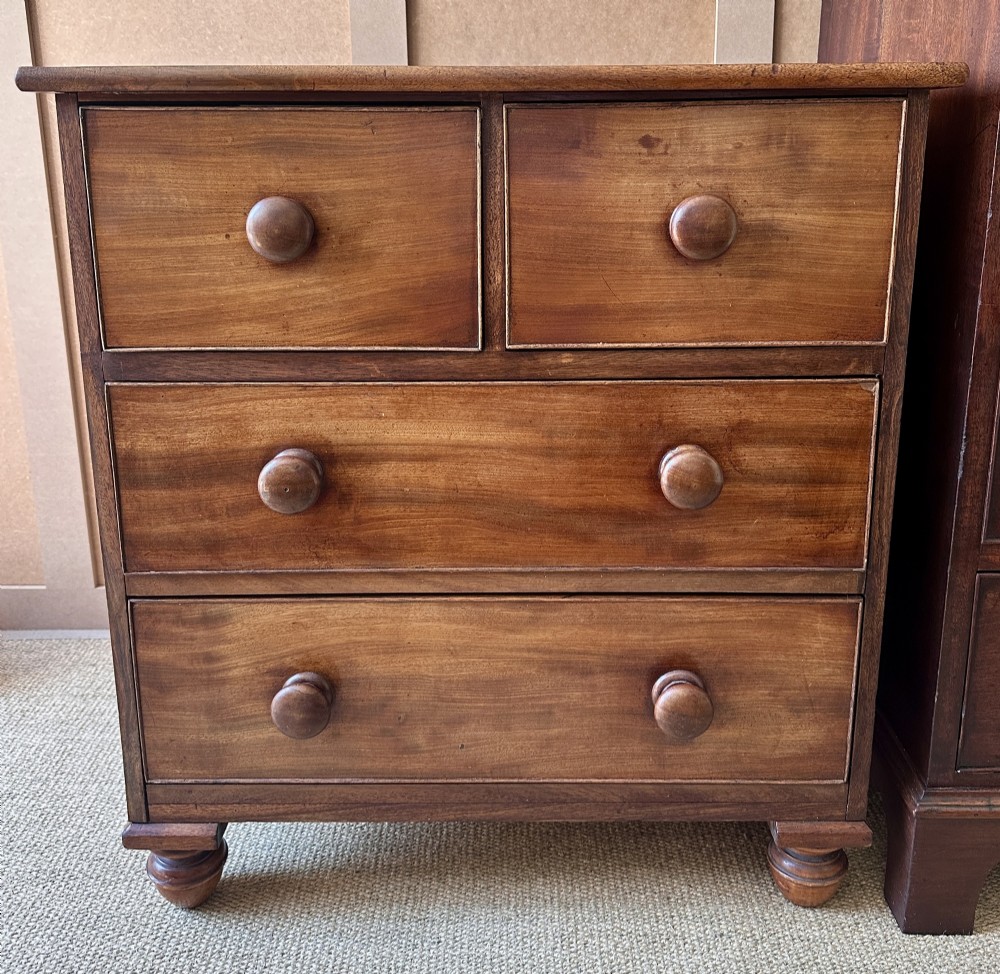 A small antique warm brown wood chest of drawers featuring two short drawers over two long drawers with turned wooden knobs and feet.