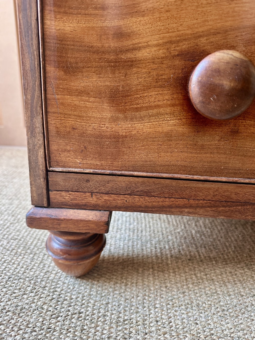 A small antique warm brown wood chest of drawers featuring two short drawers over two long drawers with turned wooden knobs and feet. View V
