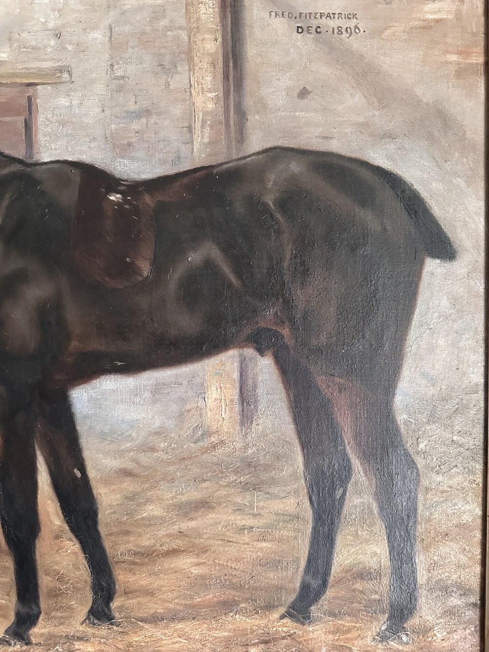 An 1896 oil painting depicting a dark brown horse standing inside a stable, housed within a gilded frame with a brass nameplate. View IV
