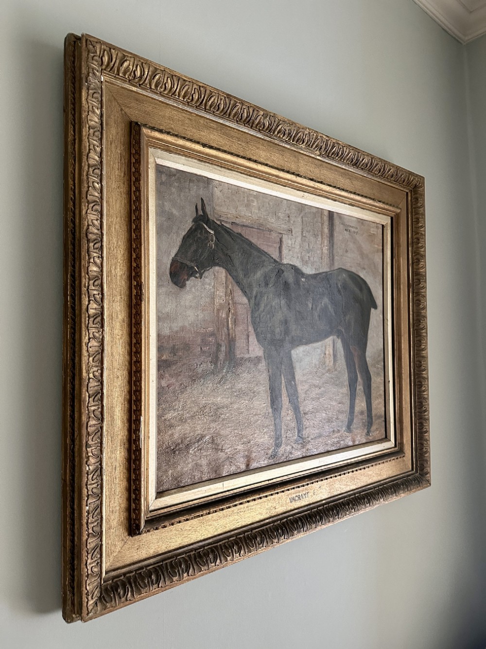 An 1896 oil painting depicting a dark brown horse standing inside a stable, housed within a gilded frame with a brass nameplate. View VIII
