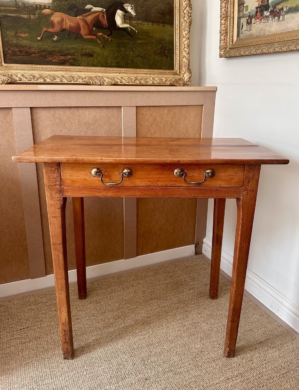 An antique pine side table featuring a single wide drawer with two brass bail handles, an overhanging rectangular top, and four square tapered legs.