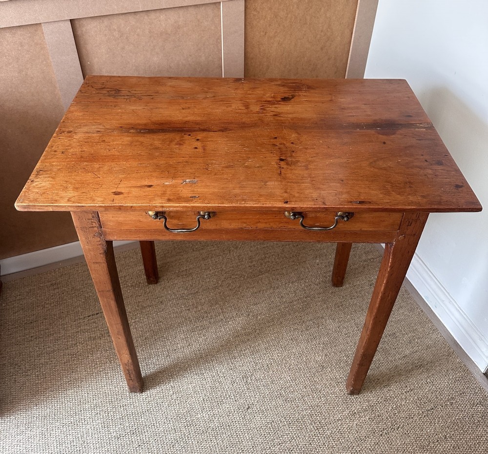 An antique pine side table featuring a single wide drawer with two brass bail handles, an overhanging rectangular top, and four square tapered legs. View II
