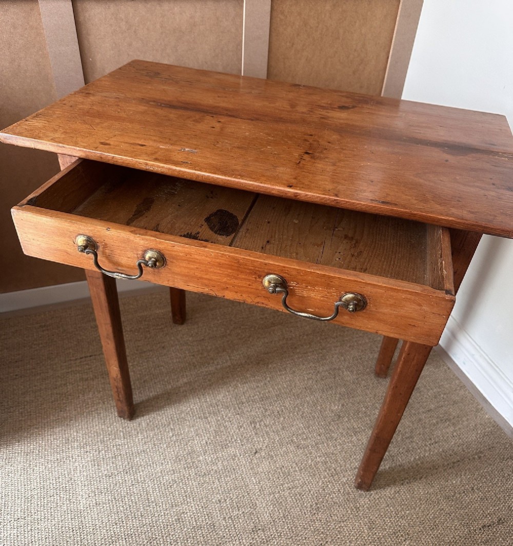 An antique pine side table featuring a single wide drawer with two brass bail handles, an overhanging rectangular top, and four square tapered legs. View IV