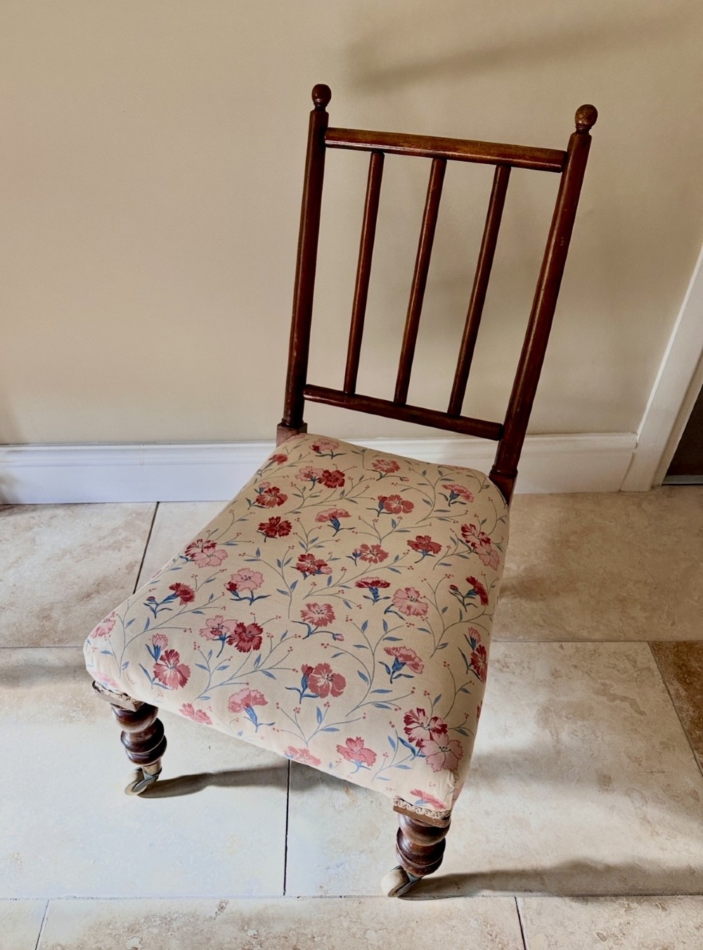 A low Victorian slipper chair featuring turned timber front legs on brass castors, a spindle back, and floral pattern textile upholstery. View IV